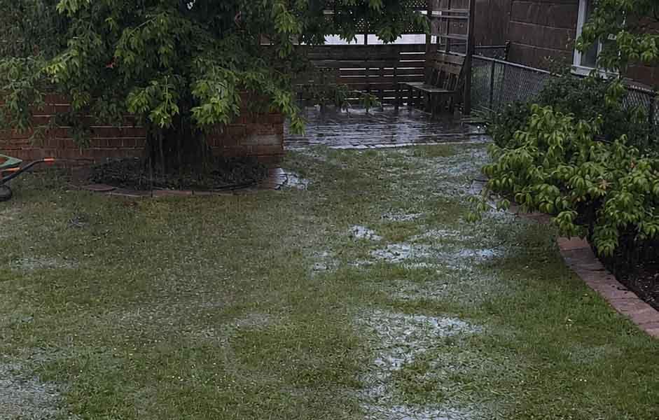 Image of someone's backyard during a rain storm. Puddles are evident on the grass, as well as a deck in the background.